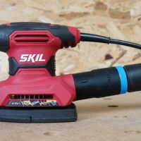 ToolCurve 27mm hose adapter attached to a red Skil orbital sander, with black dust port connector visible on the tool's rear