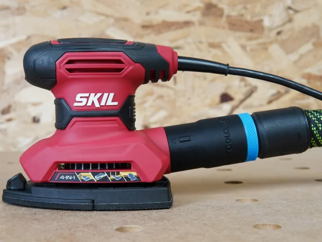 ToolCurve 27mm hose adapter attached to a red Skil orbital sander, with black dust port connector visible on the tool's rear