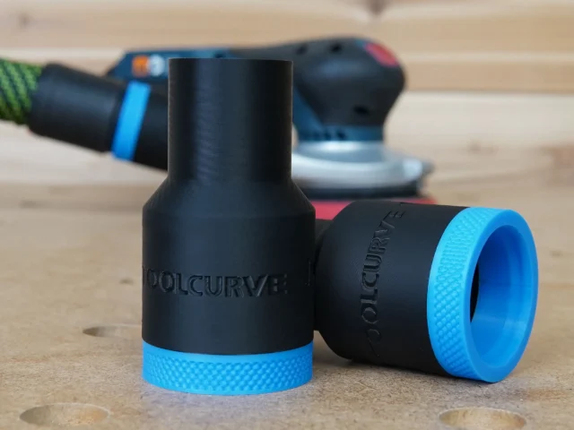 Black ToolCurve hose adapter with blue grip rings shown in pairs, one with tapered end and one with cylindrical end, in focus on wooden surface with Bosch sander blurred in background