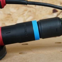 Black hose adapter with blue band attached to SKIL sander, connected to black Festool hose, shown on wooden workbench