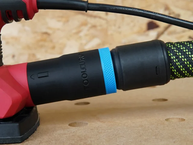 Black hose adapter with blue band attached to SKIL sander, connected to black Festool hose, shown on wooden workbench