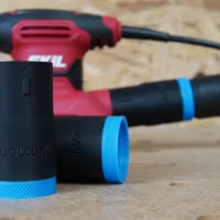 Black ToolCurve hose adapter with blue grip band, shown alone in foreground with SKIL sander in background