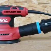 Black 1-1/4 inch hose adapter with blue band joining an orange vacuum hose to a red SKIL sander's rear dust port