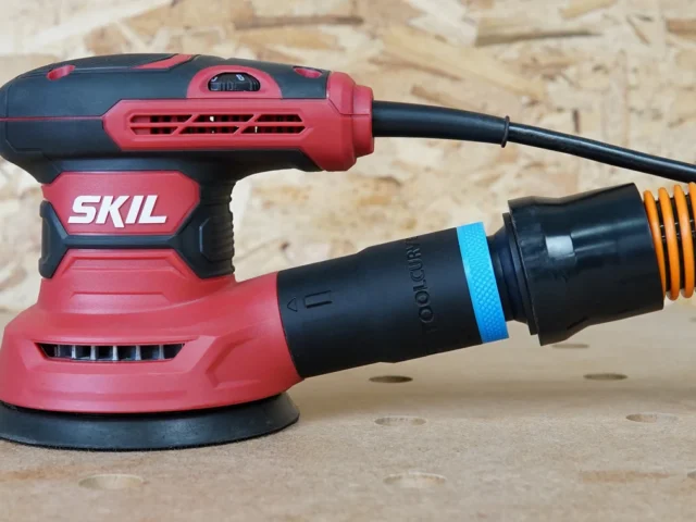 Black 1-1/4 inch hose adapter with blue band joining an orange vacuum hose to a red SKIL sander's rear dust port