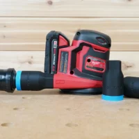 Black ToolCurve 1-1/4" hose adapter with blue collar joining an orange hose to a Milwaukee M18 sander, two spare adapters beside it