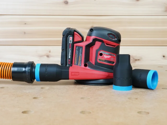 Black ToolCurve 1-1/4" hose adapter with blue collar joining an orange hose to a Milwaukee M18 sander, two spare adapters beside it