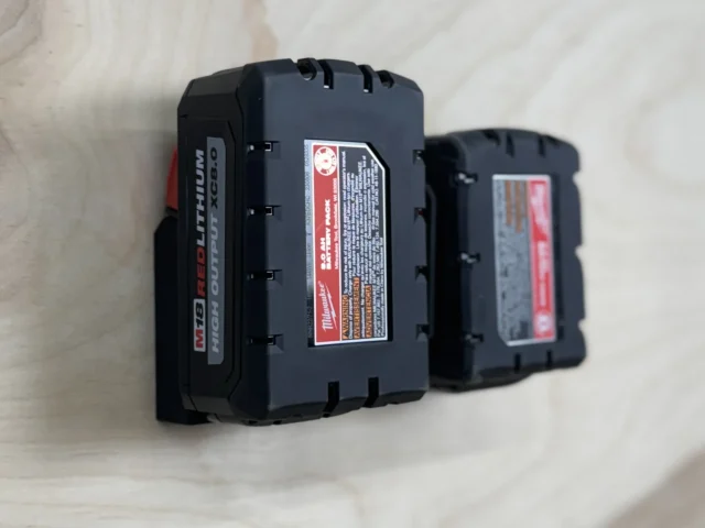 Two Milwaukee 18v batteries mounted side-by-side on a wall, showing the black plastic holder gripping each battery securely