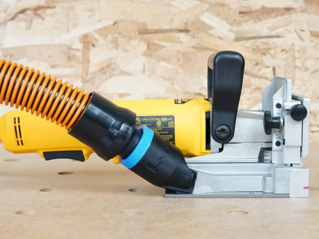 Hose adapter attached to DeWalt biscuit joiner dust port, connecting orange flex hose to white plastic mount