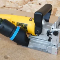 Black hose adapter attached to yellow Dewalt biscuit joiner, mounted on gray fixture with adjustment knobs and metal guides