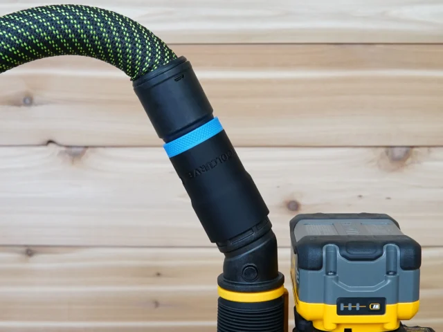 Hose adapter attached to a Dewalt 2-1/4 HP cordless plunge router, showing the black cylindrical connector with blue band and braided green hose above it, next to the yellow and blue router body.