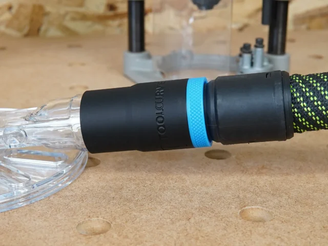 Black hose adapter with blue band connected to clear Oneida router hood dust port, with braided hose attached