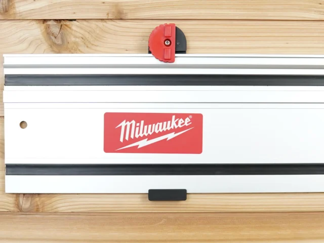 Red and black wall mount clipped onto a Milwaukee track saw rail mounted horizontally on wood