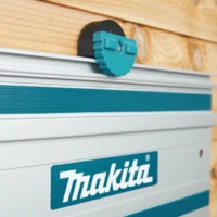 Teal and black wall mount holding a Makita guide rail against a wood-slat workshop wall, close-up view