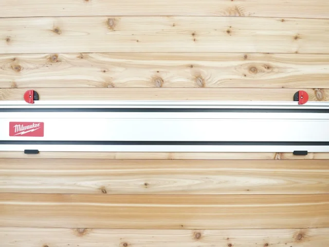 Milwaukee track saw guide rails mounted on wooden wall with red locking knobs and black mounting hardware