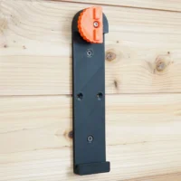 Dark gray wall-mounted rail bracket with orange locking clamp at top, mounted vertically on wood with screw holes visible