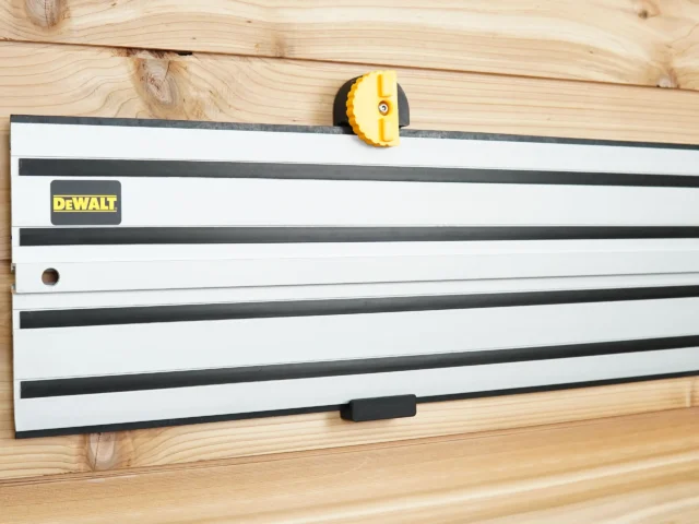 DeWalt guide rail hanging on a wood-plank wall from a black wall mount with yellow locking knob