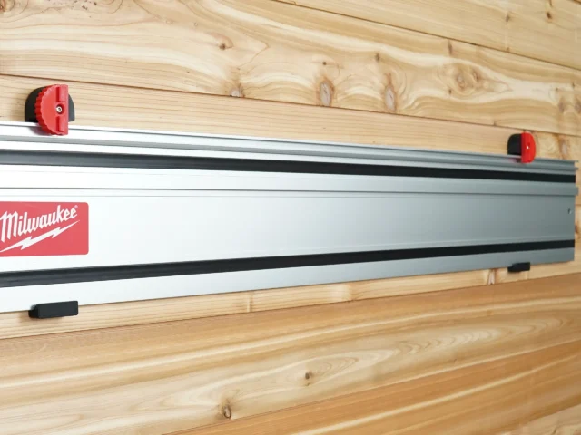 Red wall mounts securing a Milwaukee track saw rail to wooden wall studs