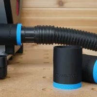 Black ToolCurve hose adapter with blue grip bands, shown alone and attached to SawStop CTS dust hose on wooden workbench