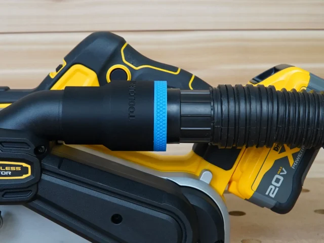 Black ToolCurve 1-7/8 inch hose adapter with blue band joining a ribbed vacuum hose to a DeWalt 20V belt sander dust port