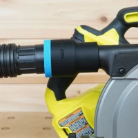 Hose adapter attached to Ryobi cordless track saw dust port, showing black cylindrical adapter body with blue band and yellow trigger handle
