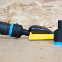 Black 36mm ToolCurve hose adapter with blue band joining a vacuum hose to a yellow Mirka hand sanding block, second adapter standing beside it