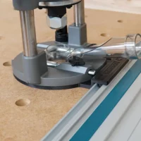 Milwaukee M18 2-1/4HP router mounted on gray guide rail adapter, positioned on a track saw rail above wood with pocket holes