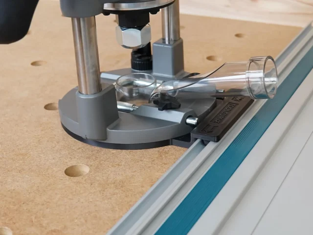 Milwaukee M18 2-1/4HP router mounted on gray guide rail adapter, positioned on a track saw rail above wood with pocket holes