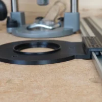 Black circular guide rail adapter mounted on Festool track rail, with gray router base visible above on wooden workbench