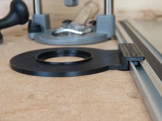 Black circular guide rail adapter mounted on Festool track rail, with gray router base visible above on wooden workbench