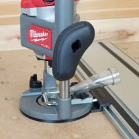 Milwaukee M18 2-1/4HP router mounted to a Kreg guide rail via gray adapter base, positioned over a wooden workbench