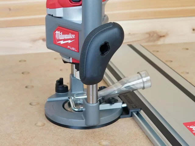 Milwaukee M18 2-1/4HP router mounted to a Kreg guide rail via gray adapter base, positioned over a wooden workbench