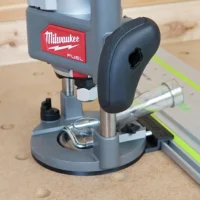 Milwaukee M18 2-1/4HP router with black rubber base plate attached to Festool guide rail, mounted on wood workbench