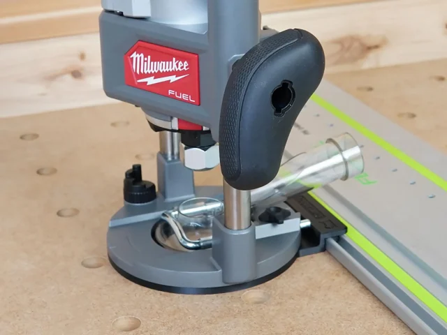 Milwaukee M18 2-1/4HP router with black rubber base plate attached to Festool guide rail, mounted on wood workbench