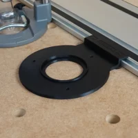 Black circular router adapter with central bore and mounting holes, positioned on pegboard next to Festool track rail