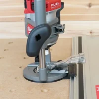 Milwaukee M18 router with guide rail adapter mounted on Kreg track rail, positioned over wooden workpiece with pocket holes