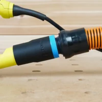 Black ToolCurve 1-1/4" hose adapter with blue band linking a yellow Ryobi sander port to an orange hose