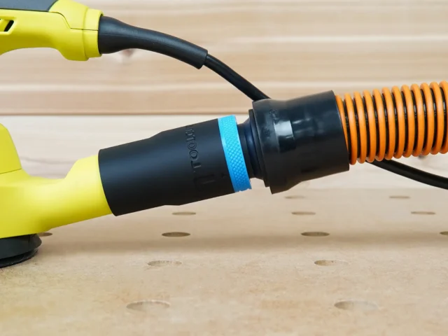 Black ToolCurve 1-1/4" hose adapter with blue band linking a yellow Ryobi sander port to an orange hose