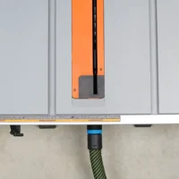 Orange and black hose adapter attached to Ridgid portable table saw's rear dust port, with green-wrapped hose connected below