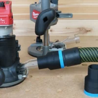 Black ToolCurve 36mm hose adapter with blue band joining a vacuum hose beside a Milwaukee M18 router