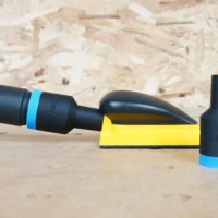 Black ToolCurve hose adapter with blue band joining an extractor hose to a yellow Mirka hand sanding block, second adapter standing alongside