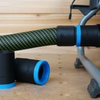 Black 36mm ToolCurve hose adapter with blue ring joining a green hose to a Ridgid table saw dust port, two spare adapters on the bench