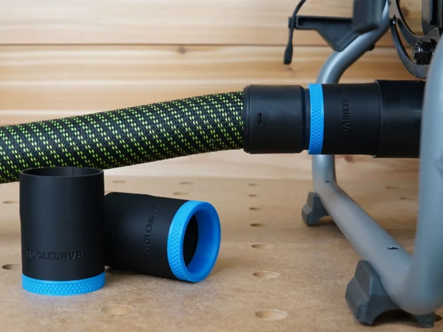 Black 36mm ToolCurve hose adapter with blue ring joining a green hose to a Ridgid table saw dust port, two spare adapters on the bench