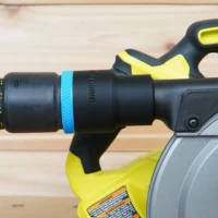 ToolCurve hose adapter attached to Ryobi cordless track saw dust port, showing black cylindrical body with blue band and yellow grip handles
