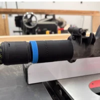Black hose adapter with blue band attached to SawStop table saw blade guard dust port, shown in workshop