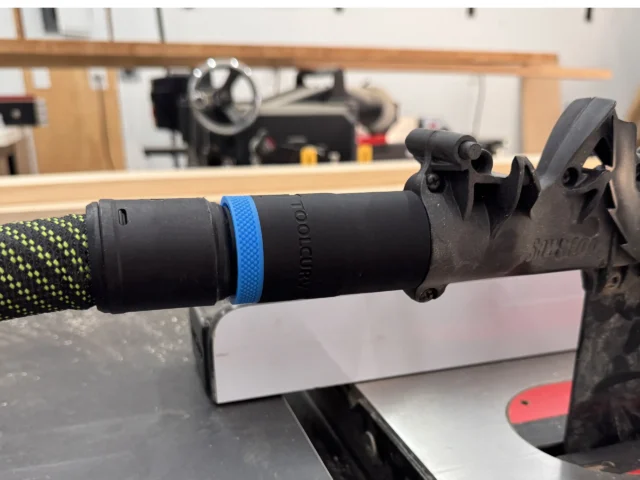 Black hose adapter with blue band attached to SawStop table saw blade guard dust port, shown in workshop