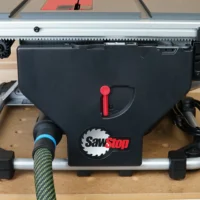 Hose adapter attached to rear dust port of SawStop Compact table saw, showing black plastic body with red lever handle and connected green-jacketed hose