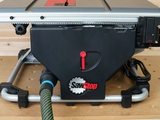 Hose adapter attached to rear dust port of SawStop Compact table saw, showing black plastic body with red lever handle and connected green-jacketed hose