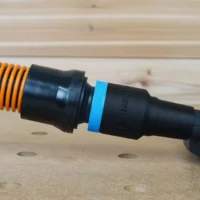 Black 1-1/4 inch hose adapter with blue ring joining an orange vacuum hose to a Dewalt disc sander port