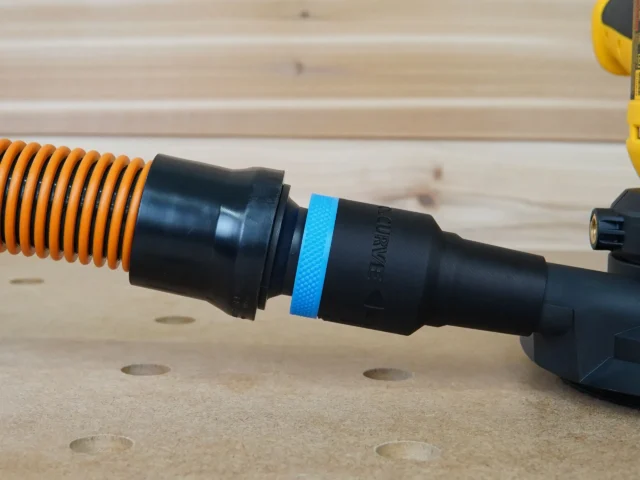 Black 1-1/4 inch hose adapter with blue ring joining an orange vacuum hose to a Dewalt disc sander port