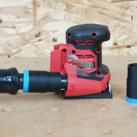 Black 1-1/4 inch ToolCurve hose adapter with blue band joining an orange hose to a Milwaukee sheet sander, spare adapter beside